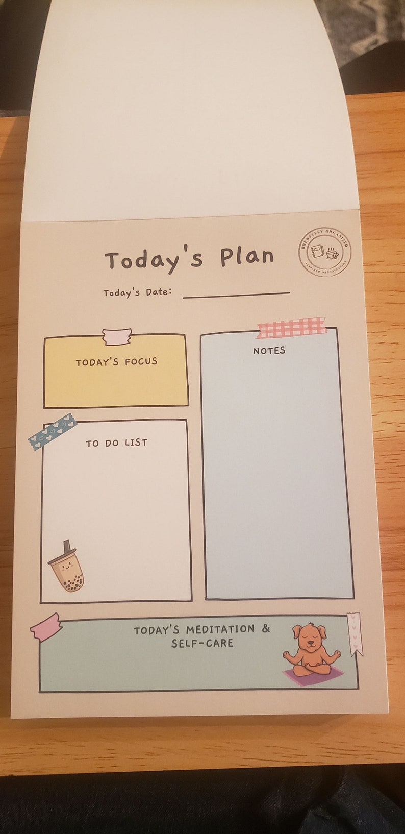 May include: A beige planner with a light brown border and the text "Today's Plan" in black. The planner has sections for "Today's Focus", "Notes", "To Do List", and "Today's Meditation & Self-Care". Each section has a decorative border and a small illustration.