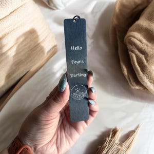 Puede incluir: Marcapáginas de madera negro con un diseño de montaña blanco y las palabras "Hello Feyre Darling" grabadas.