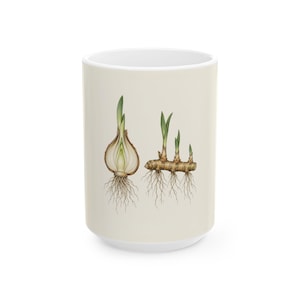 Könnte beinhalten: Ein cremefarbener Keramikbecher mit einer detaillierten botanischen Illustration einer aufgeschnittenen Zwiebel mit Wurzeln auf der linken Seite und einem Ingwer-Rhizom mit grünen Trieben und faserigen Wurzeln auf der rechten Seite.