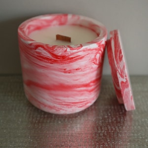 May include: A red and white marbled candle jar with a wooden wick and a matching lid.
