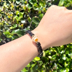 May include: A black wooden bracelet with a white paw print charm. The bracelet is on a person's wrist.