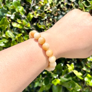 May include: A bracelet made of light brown and white round beads. The bracelet is on a person's wrist.