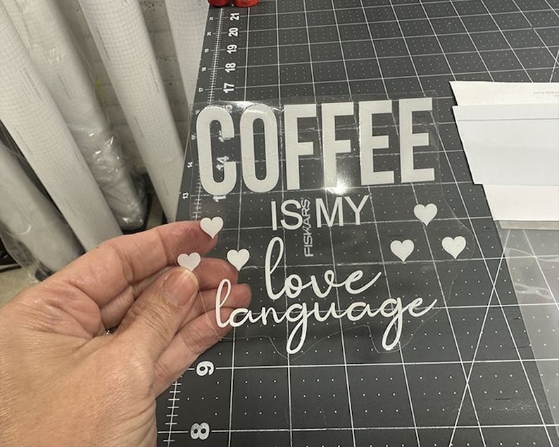 K&ouml;nnte beinhalten: Wei&szlig;er Vinyl-Aufkleber mit dem Text "Coffee is my love language" mit kleinen Herzen um den Text. Der Aufkleber ist auf einem transparenten Hintergrund.