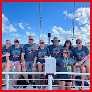 May include: A group of people wearing matching gray t-shirts with the text "CANCUN 2022" and sunglasses graphics. They are standing on a boat deck with a blue sky and white clouds in the background.