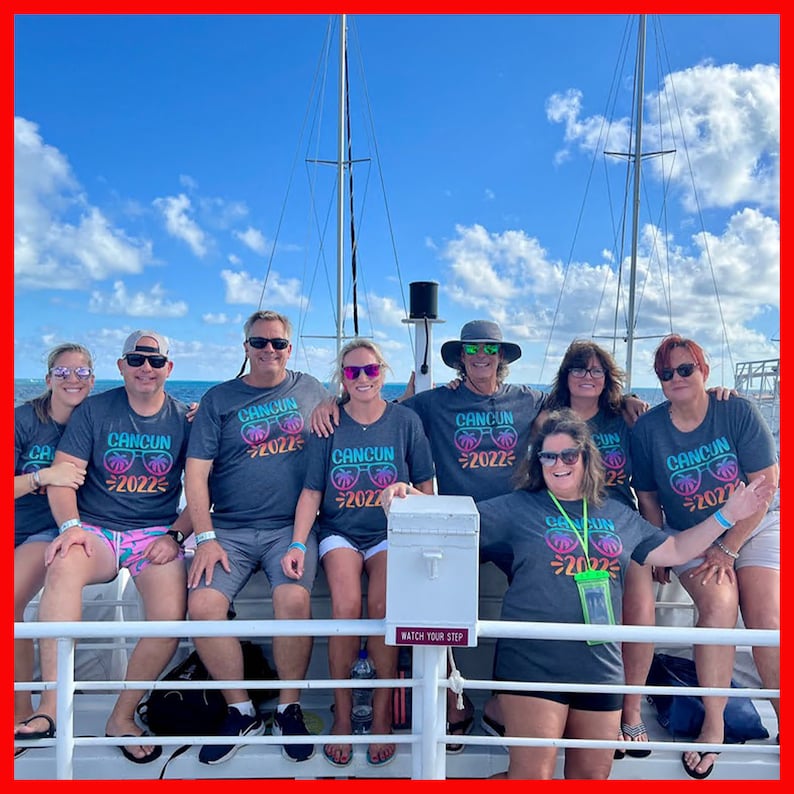 May include: A group of people wearing matching gray t-shirts with the text "CANCUN 2022" and sunglasses graphics. They are standing on a boat deck with a blue sky and white clouds in the background.