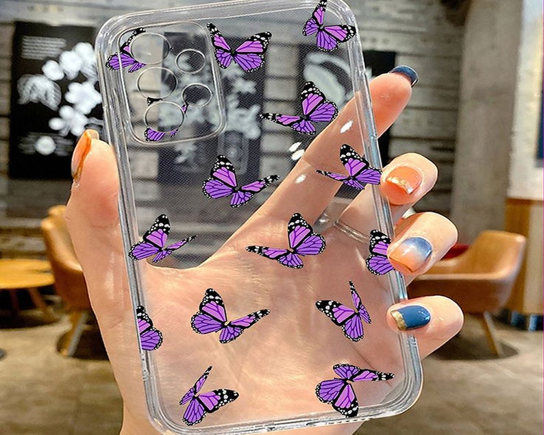 K&ouml;nnte beinhalten: Eine transparente Handyh&uuml;lle mit einem Muster aus lila Schmetterlingen. Die H&uuml;lle ist f&uuml;r ein Smartphone mit einer Kamerabuckel konzipiert.