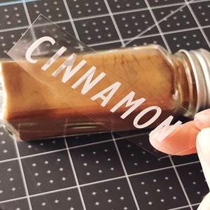 K&ouml;nnte beinhalten: Ein klares Glasgef&auml;&szlig; mit einem silbernen Deckel, gef&uuml;llt mit braunem Zimt. Ein klares Etikett mit dem Wort "CINNAMON" wird auf das Gef&auml;&szlig; geklebt.