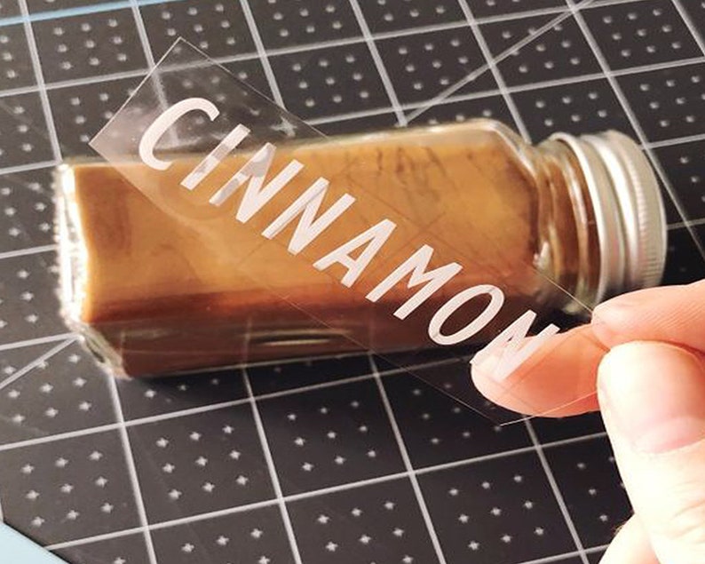 K&ouml;nnte beinhalten: Ein klares Glasgef&auml;&szlig; mit einem silbernen Deckel, gef&uuml;llt mit braunem Zimt. Ein klares Etikett mit dem Wort "CINNAMON" wird auf das Gef&auml;&szlig; geklebt.