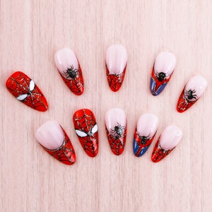 Puede incluir: Diez puntas de u&ntilde;as rojas y negras con un dise&ntilde;o de telara&ntilde;a. Las puntas de las u&ntilde;as est&aacute;n decoradas con una telara&ntilde;a negra y una ara&ntilde;a negra.