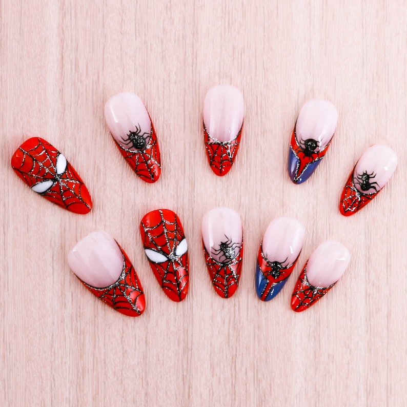 Puede incluir: Diez puntas de u&ntilde;as rojas y negras con un dise&ntilde;o de telara&ntilde;a. Las puntas de las u&ntilde;as est&aacute;n decoradas con una telara&ntilde;a negra y una ara&ntilde;a negra.