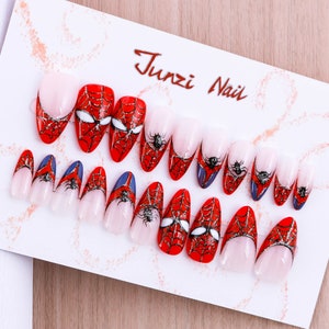 Puede incluir: Un conjunto de 12 u&ntilde;as postizas con un dise&ntilde;o de telara&ntilde;a roja y negra. Las u&ntilde;as son de forma ovalada y tienen un acabado brillante. El dise&ntilde;o presenta una telara&ntilde;a con una ara&ntilde;a en el centro. El texto "Junzi Nail" est&aacute; impreso en la tarjeta blanca.