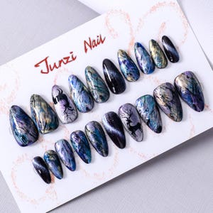 Puede incluir: Conjunto de 10 uñas postizas con un diseño abstracto negro, azul y plateado con una silueta de ciervo. Las uñas tienen una forma larga y de almendra. Las uñas están etiquetadas como "Junzi Nail".