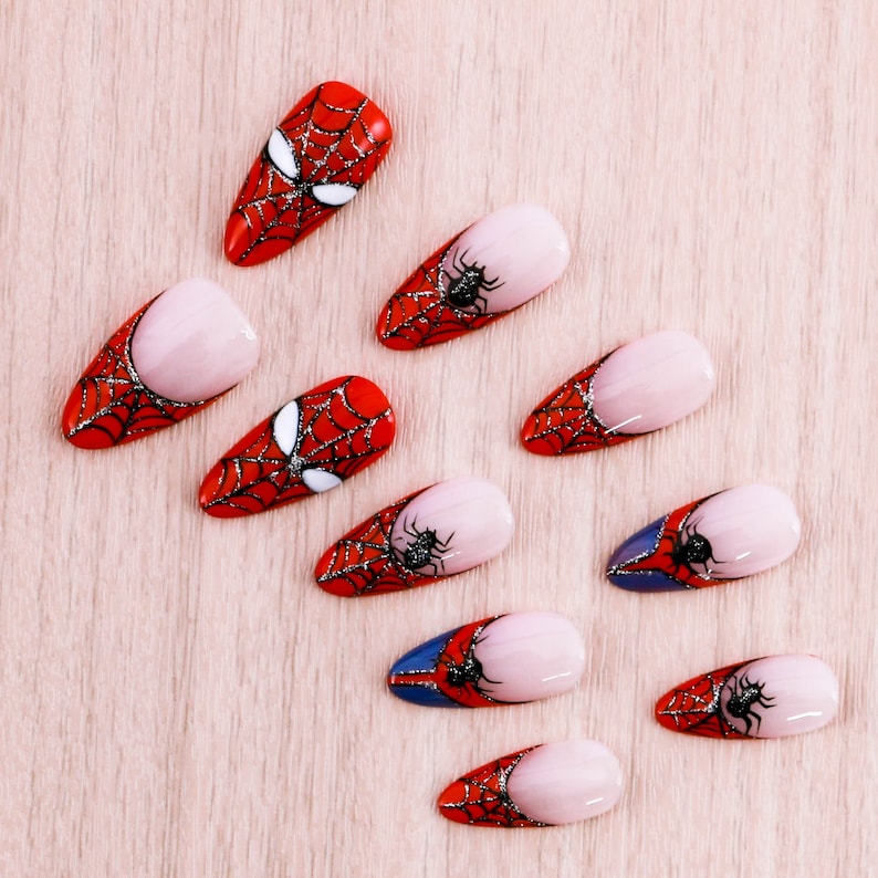 Puede incluir: Diez dise&ntilde;os de arte de u&ntilde;as rojas y blancas con un patr&oacute;n de ara&ntilde;a y telara&ntilde;a. Los dise&ntilde;os est&aacute;n sobre un fondo de madera claro.