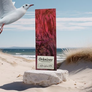 May include: A close-up of a piece of wood with a pink and purple marbled pattern. The wood is 32 inches by 46 inches by 139 inches. The wood is labeled "Orknives".