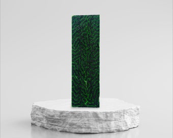 May include: A green and black patterned rectangular block standing on a white platform. The block has a textured surface with a green pattern on a black background.