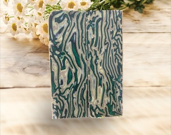 May include: Two pieces of green and gold marbled wood with a swirling pattern. The wood is cut into rectangular shapes.