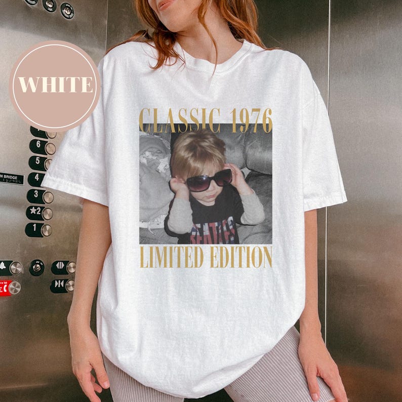 May include: White t-shirt with a photo of a child wearing sunglasses, with the text "CLASSIC 1976" and "LIMITED EDITION" in gold. The shirt has a crew neck and short sleeves.