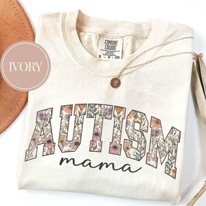 May include: Ivory t-shirt with a floral design spelling out "AUTISM mama".