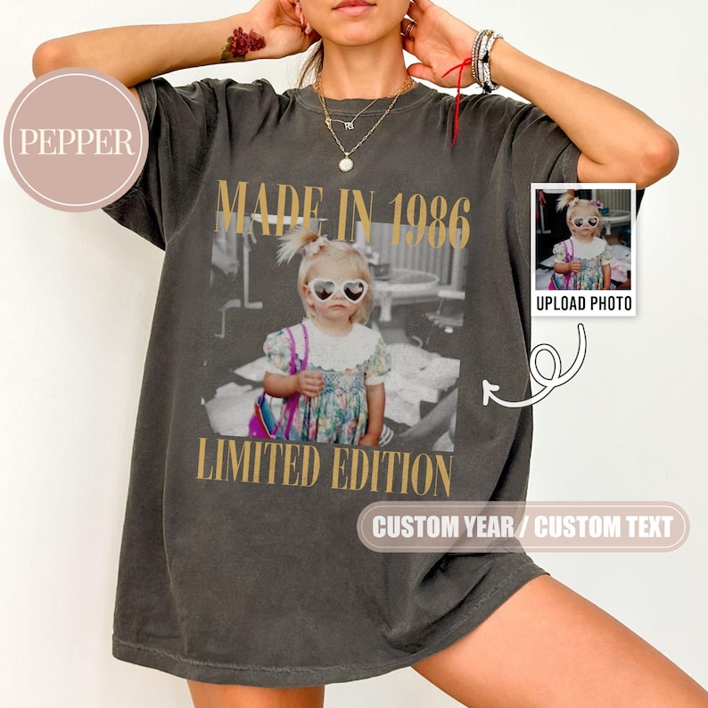 May include: Dark gray t-shirt with a vintage photo print. The photo features a child wearing heart-shaped sunglasses. Gold text reads "MADE IN 1986" and "LIMITED EDITION". A small photo is on the right with the text "UPLOAD PHOTO".