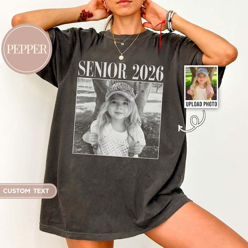 May include: Dark grey t-shirt featuring the text "SENIOR 2026" above a black and white photograph of a child. The shirt has a faded, vintage appearance. A small photo with the text "UPLOAD PHOTO" is on the right.
