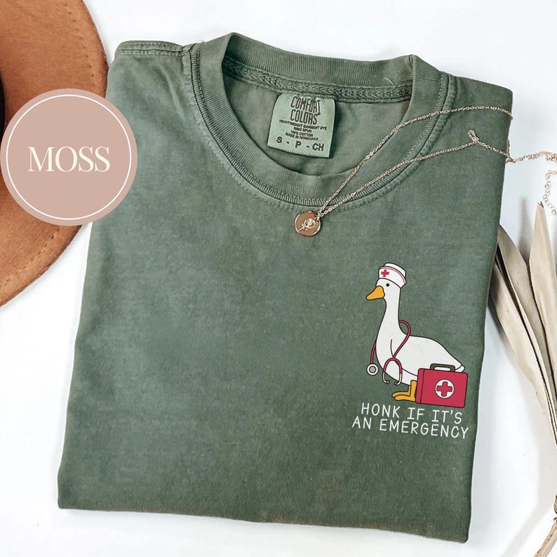 May include: A green t-shirt with a cartoon image of a goose wearing a nurse's hat and holding a stethoscope and a first aid kit. The text "Honk if it's an emergency" is printed below the image.