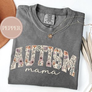 May include: Gray t-shirt with a floral print design that spells out "AUTISM mama".