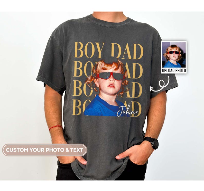 Pode incluir: T-shirt cinzento escuro com as palavras douradas "BOY DAD". A camisa apresenta uma foto de uma crian&ccedil;a usando &oacute;culos de sol. O nome "Johan" est&aacute; escrito abaixo da foto. Uma pequena foto est&aacute; no canto superior direito com o texto "UPLOAD PHOTO".
