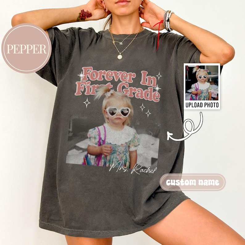 K&ouml;nnte beinhalten: Dunkelgraues T-Shirt mit einem Foto eines Kindes mit herzf&ouml;rmiger Sonnenbrille. Der Text "Forever In First Grade" steht in Rosa und Wei&szlig; &uuml;ber dem Foto. Das Shirt hat auch ein kleines Foto und den Text "Upload Photo" und "custom name".
