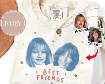 Può includere: T-shirt color avorio con due ritratti in tonalità blu e la scritta rosa "BEST FRIENDS". La maglietta presenta un piccolo motivo a stelle e due inserti fotografici con l'etichetta "YOUR PHOTO". Una collana d'oro è drappeggiata sulla maglietta.