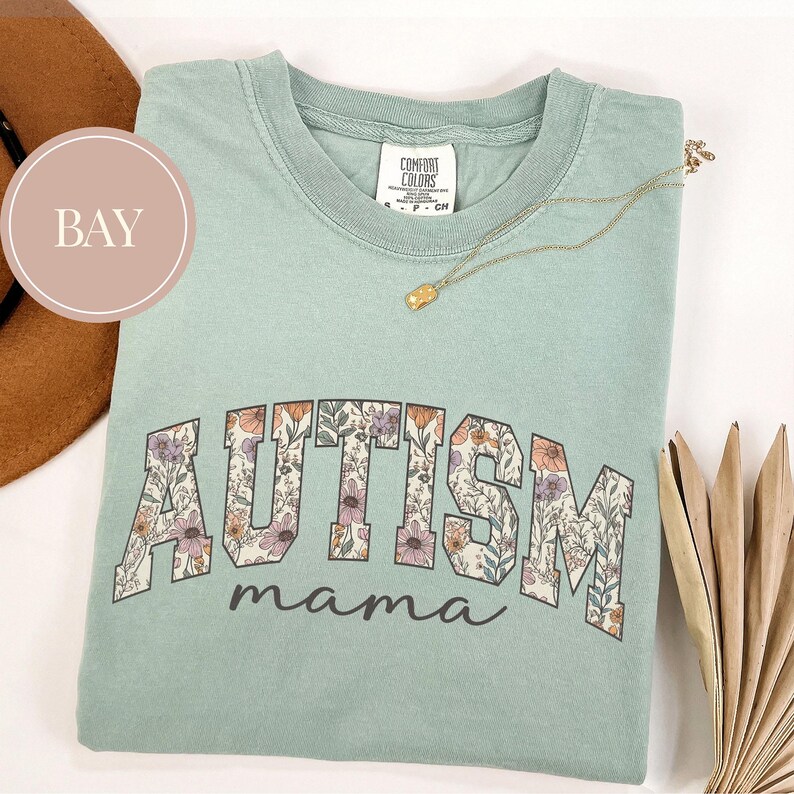 May include: A light green t-shirt with a floral print of the word "AUTISM" and the text "mama" underneath.