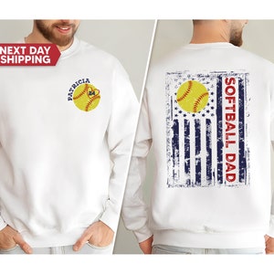 May include: White sweatshirt with a softball design on the front and a distressed American flag with the text "Softball Dad" on the back.