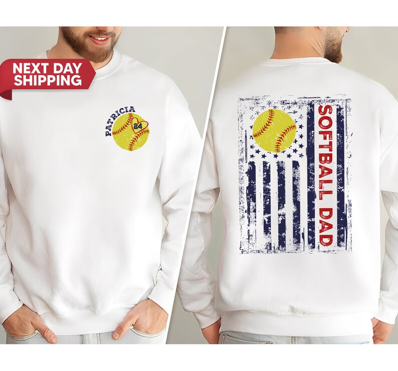 May include: White sweatshirt with a softball design on the front and a distressed American flag with the text "Softball Dad" on the back.