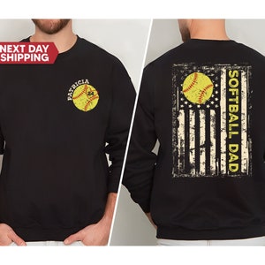 May include: Black sweatshirt with a distressed American flag design featuring a softball and the text "Softball Dad". The front of the sweatshirt has a softball with the text "Patricia" above it.