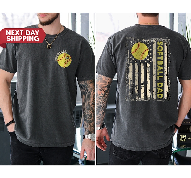 May include: A black t-shirt with a distressed American flag design featuring a softball and the text "Softball Dad". The front of the shirt has a softball with the text "Patricia" on it.