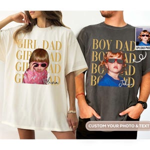 Pode incluir: Duas camisetas grandes, uma creme e outra cinza carv&atilde;o, com estampas fotogr&aacute;ficas personalizadas. A camiseta creme diz "GIRL DAD" com uma foto de uma crian&ccedil;a usando &oacute;culos de sol. A camiseta cinza diz "BOY DAD".