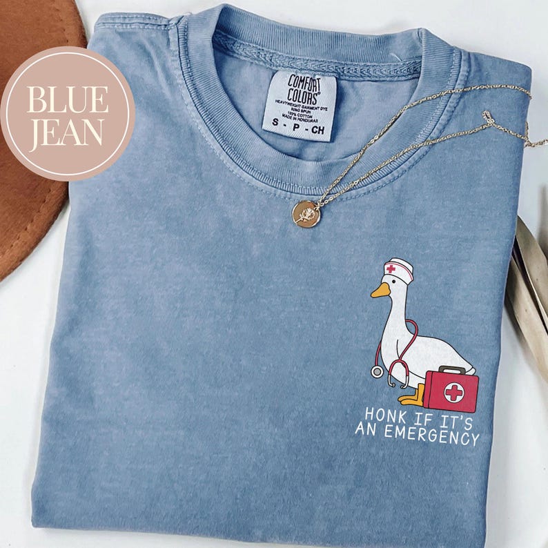 May include: A blue jean t-shirt with a white cartoon goose wearing a nurse's hat and holding a stethoscope. The text "Honk if it's an emergency" is printed below the goose.