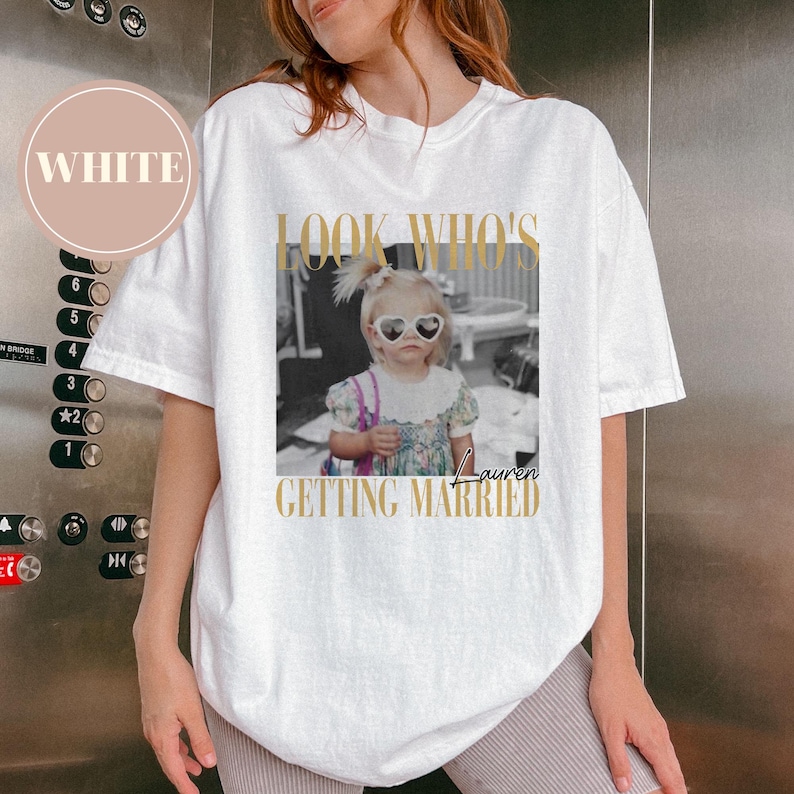 May include: White t-shirt with a graphic that says "LOOK WHO'S GETTING MARRIED" with a black and white photo of a child wearing heart-shaped sunglasses. The word "Lauren" is below the photo.