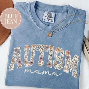 May include: A light blue t-shirt with a floral design spelling out "AUTISM mama".