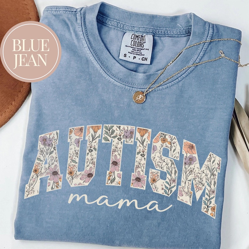 May include: A light blue t-shirt with a floral design spelling out "AUTISM mama".