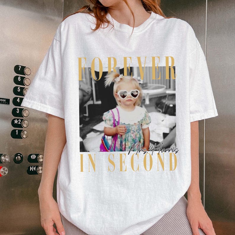 K&ouml;nnte beinhalten: Wei&szlig;es T-Shirt mit einem Schwarz-Wei&szlig;-Foto eines kleinen M&auml;dchens mit herzf&ouml;rmiger Sonnenbrille. Der goldfarbene Text "FOREVER IN SECOND" umrahmt das Bild, mit "Mrs. Harris" in Schreibschrift.