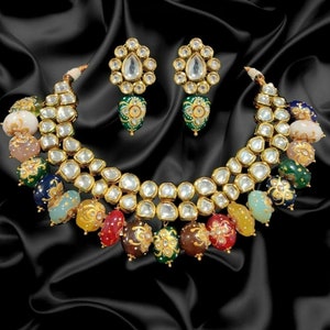 May include: A gold necklace with a double row of clear stones and colourful beads. The necklace is accented with gold and green floral designs. Matching earrings with clear stones and green floral designs are also included.