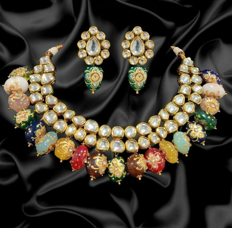 May include: A gold necklace with a double row of clear stones and colourful beads. The necklace is accented with gold and green floral designs. Matching earrings with clear stones and green floral designs are also included.