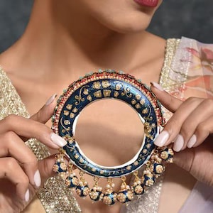 May include: A blue and gold bangle with white enamel and pearl accents. The bangle is decorated with intricate floral designs and has a dangling chain of blue and gold beads.