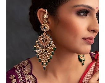 May include: Gold and green dangle earrings with a teardrop shape. The earrings feature intricate details and are adorned with pearls and green stones.