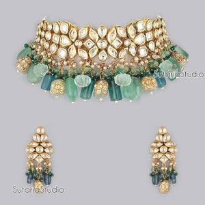 May include: A gold and green necklace and earrings set featuring a floral design and green gemstone accents. The necklace has a large, ornate pendant with a floral design and is accented with green gemstones. The earrings are smaller and have a similar floral design with green gemstone accents. The set is made of gold and green gemstones.