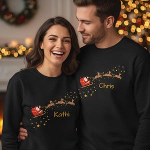 May include: Black sweatshirts featuring a Santa Claus sleigh design with the names "Kathi" and "Chris" in gold lettering. The design includes a red sleigh, reindeer, and gold stars, perfect for the holiday season.