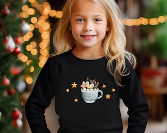 May include: Black sweatshirt featuring a whimsical Christmas design. The graphic includes a penguin in a mug of hot cocoa, gingerbread cookies, cinnamon sticks, and the text "Merry Christmas" with star accents.