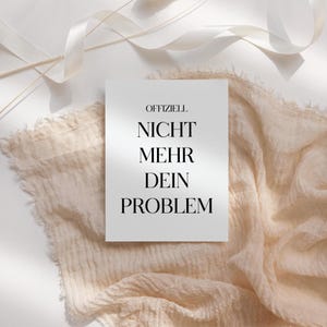 Könnte beinhalten: Eine weiße Karte mit dem Text "OFFIZIELL NICHT MEHR DEIN PROBLEM" in Schwarz, vor einem Hintergrund aus beigem Stoff und weißen Bändern. Die Karte ist der Mittelpunkt, mit deutlich lesbarem Text.