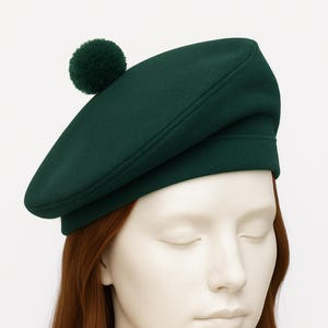 May include: A dark green beret with a matching pom-pom on top. The hat is made of a soft material and has a classic, stylish design. The beret is a timeless accessory.