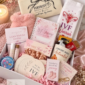 May include: A white gift box containing an IVF care package with a canvas pouch labelled Fertility Medication, a notebook titled This IVF Journey, socks with a uterus graphic, a mug saying Comfort Mode: Activated, and various cards with text including We're Having IVF and A Little Wish For Fertility.